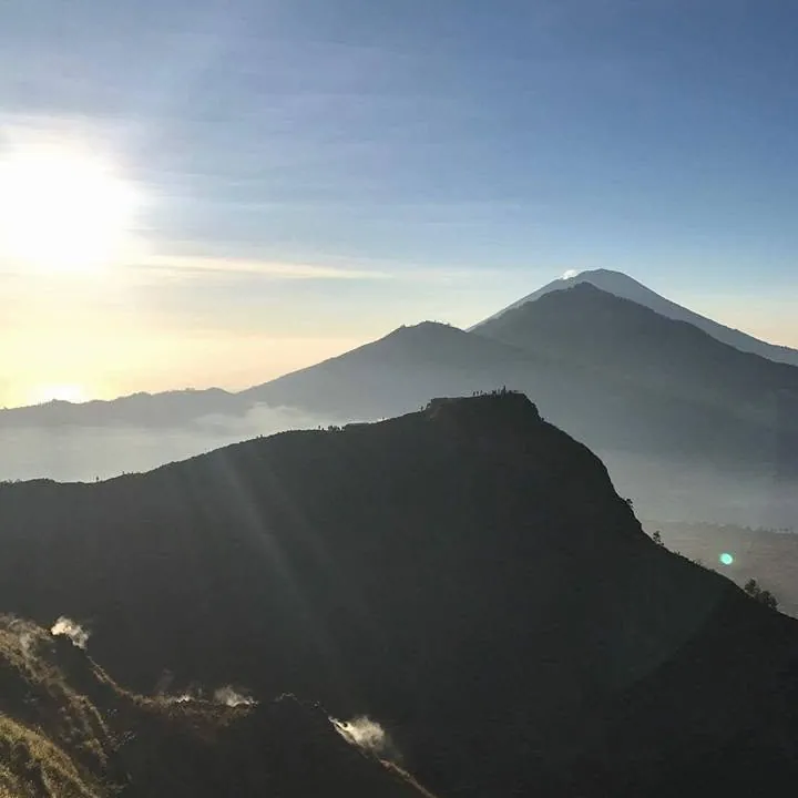 Mount Batur silhouetted against a glowing sky above the clouds